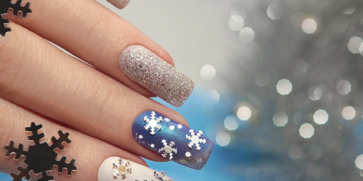 Square nails with blue snowflake art, silver glitter and a white accent nail beside silver snowflake confetti