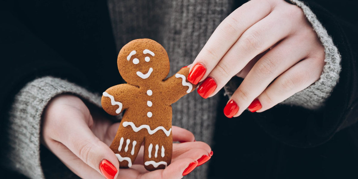 Hands with glossy red nails holding a gingerbread man cookie with white icing