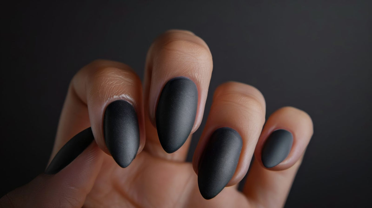 Hand with matte black almond nails against a dark background