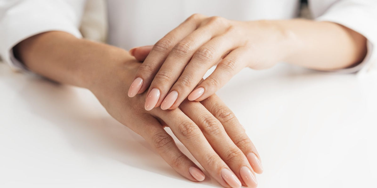 Two hands resting on a white table with neat nude-peach manicured nails