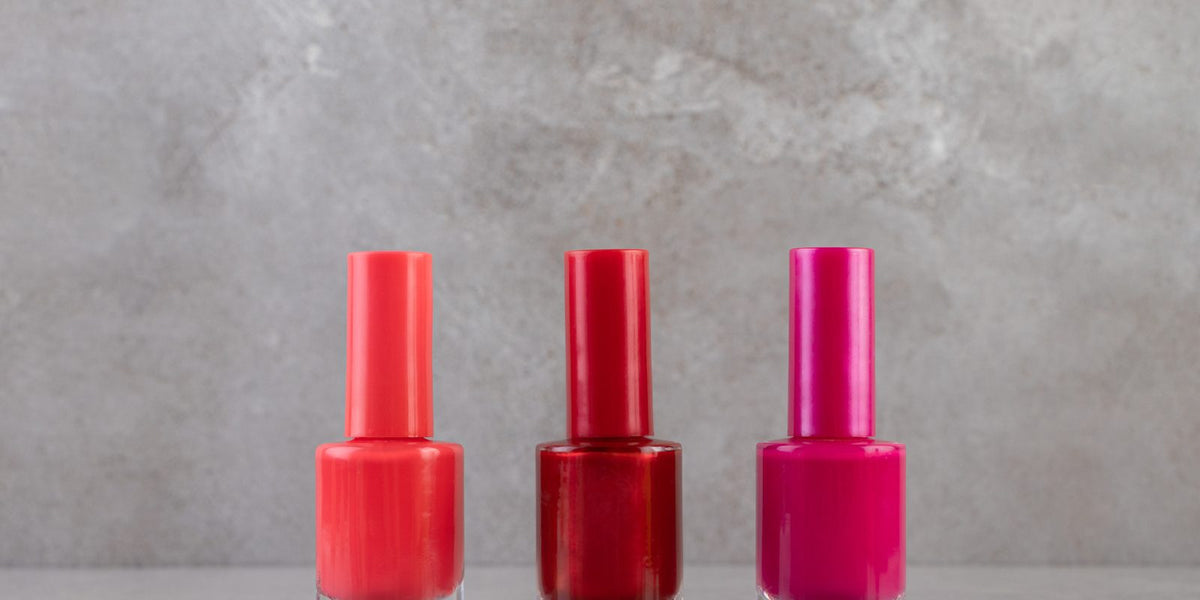 Three bottles of nail polish in red, dark red and pink on a gray stone table