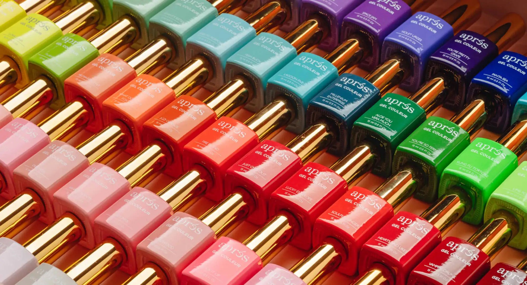 Rows of vibrant, glossy aprés nail polish bottles in assorted colors with gold caps.