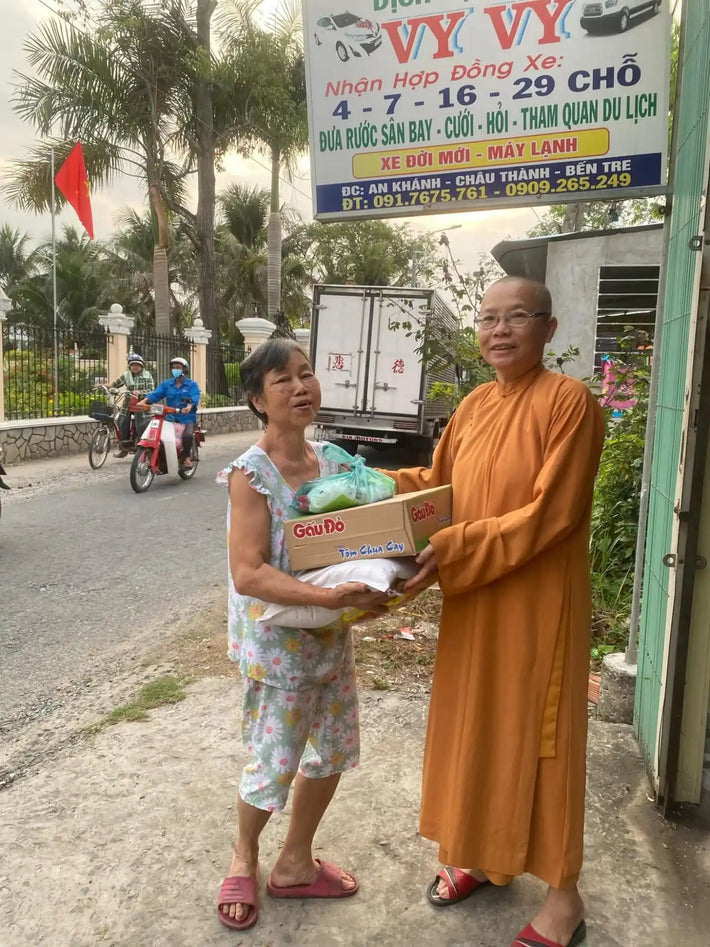 Two women, one in a monk’s robe, exchanging a box and a bag of goods.